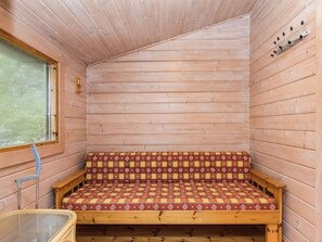 Puinen mökki sisältä, jossa on penkki, ikkuna ja seinään kiinnitetty koukku.