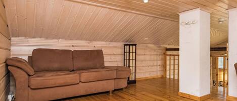A room with a wooden ceiling, a brown sofa, a white rug, and a wooden floor.