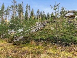 Eine Holztreppe führt einen Hügel hinauf, umgeben von dichtem Wald und einem Gebäude mit einem geneigten Dach.
