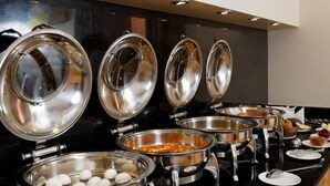 A buffet setup with multiple stainless steel serving dishes and lids, arranged on a black countertop. - Silver Oak @43 (Gurugram)