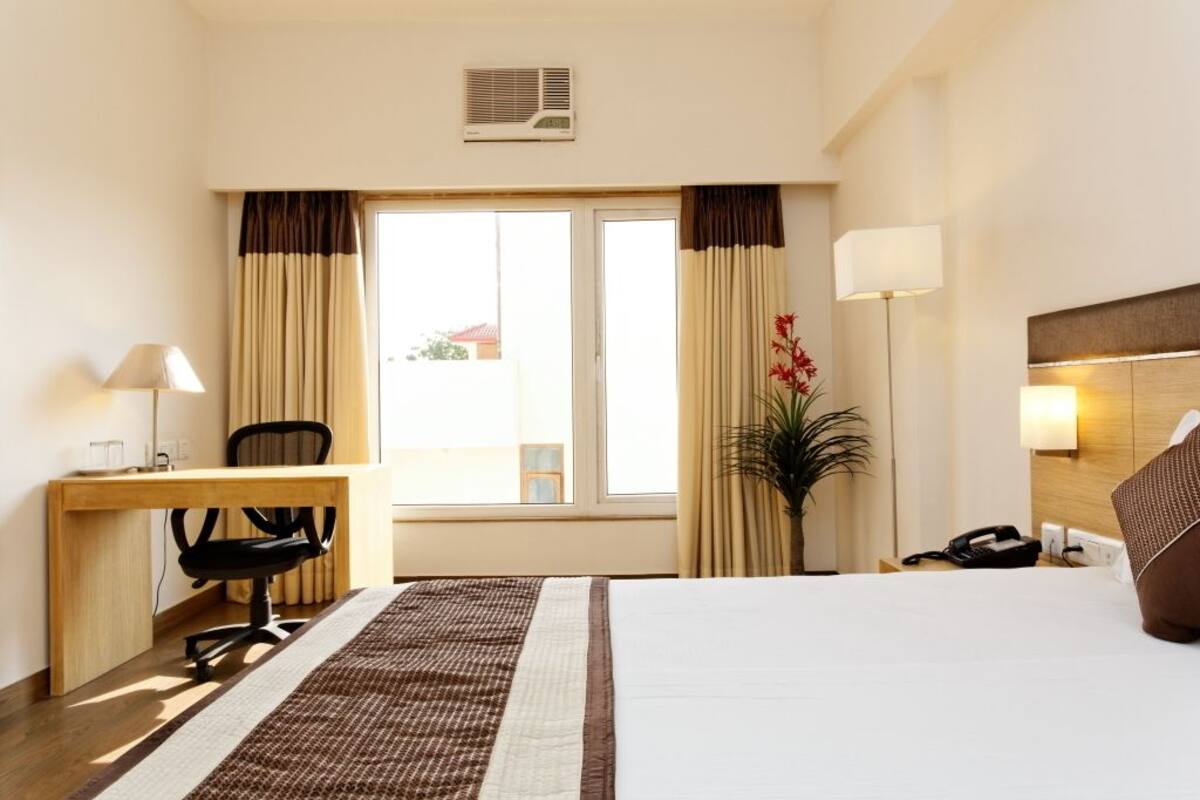 A hotel room with a bed, desk, chair, lamp, and a potted plant.