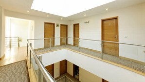 A multi-level hotel interior with a central atrium, wooden doors, and a glass railing on the upper level. - Silver Oak @43 (Gurugram)