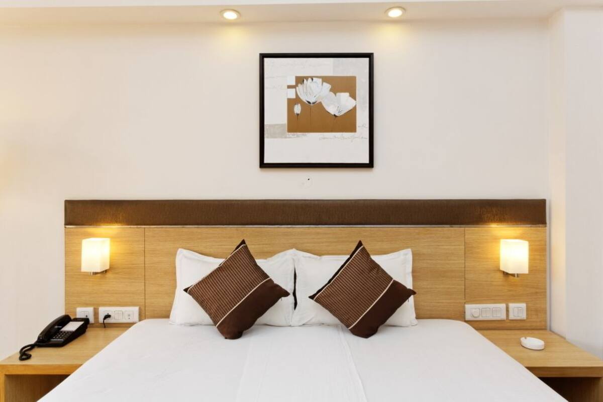 A hotel room with a wooden headboard, two bedside lamps, a framed artwork above the bed, and a telephone on the nightstand.