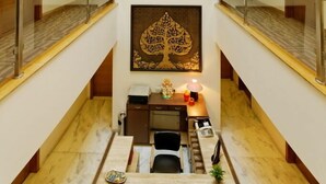 A hotel lobby with a central staircase, wooden doors, a desk with a lamp, and a decorative tree artwork. - Silver Oak @43 (Gurugram)