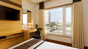 A hotel room with a bed, a desk with a chair, a TV mounted on the wall, and a large window with curtains. - Silver Oak @43 (Gurugram)