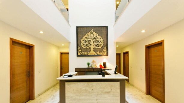 A hotel lobby with a central reception desk, wooden doors on either side, and a large decorative wall piece above the desk. - Silver Oak @43 (Gurugram)