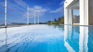 A clear blue swimming pool with a view of mountains and a modern building with large windows. - The Mare Pool Villa Pension (Taean)