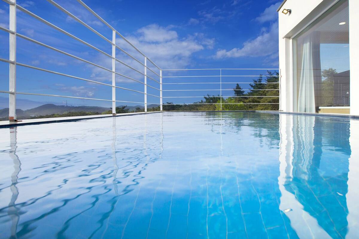 A clear blue swimming pool with a view of mountains and a modern building with large windows.
