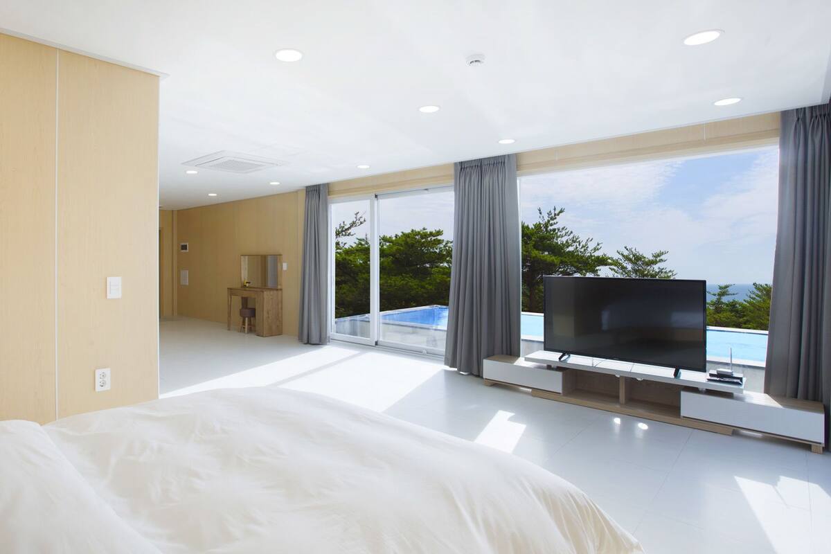 A hotel room with a large bed, a TV, and a view of a swimming pool and greenery.