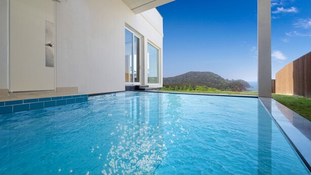 A modern swimming pool with clear blue water, a wooden deck, and a view of a mountainous landscape. - The Mare Pool Villa Pension (Taean)
