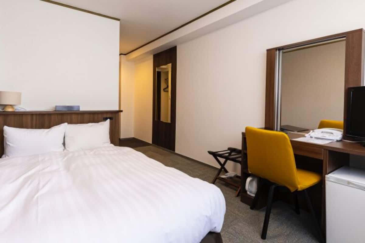 A hotel room with a bed, a desk with a chair, a television, and a refrigerator.