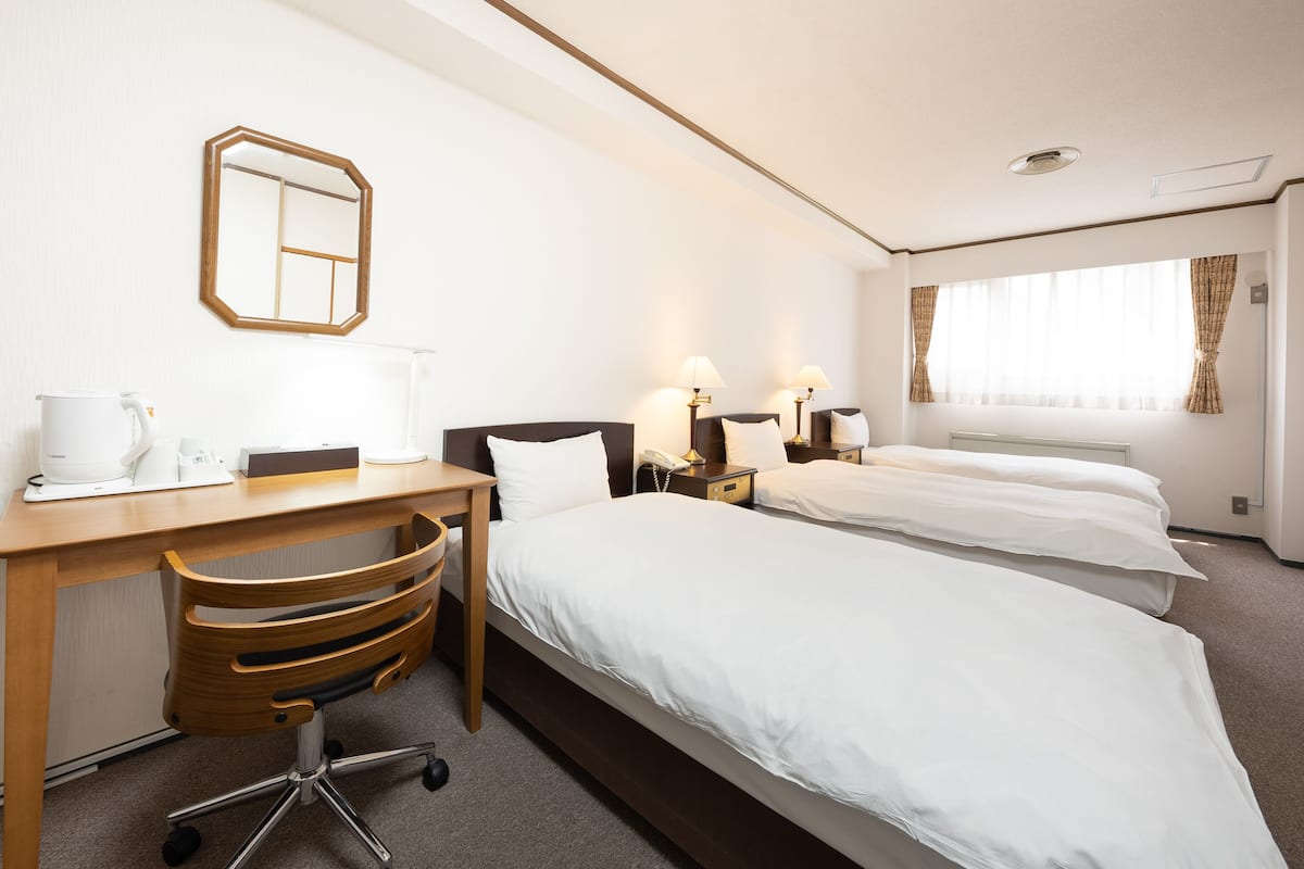 A hotel room with two beds, a desk with a chair, a coffee maker, and a mirror on the wall.