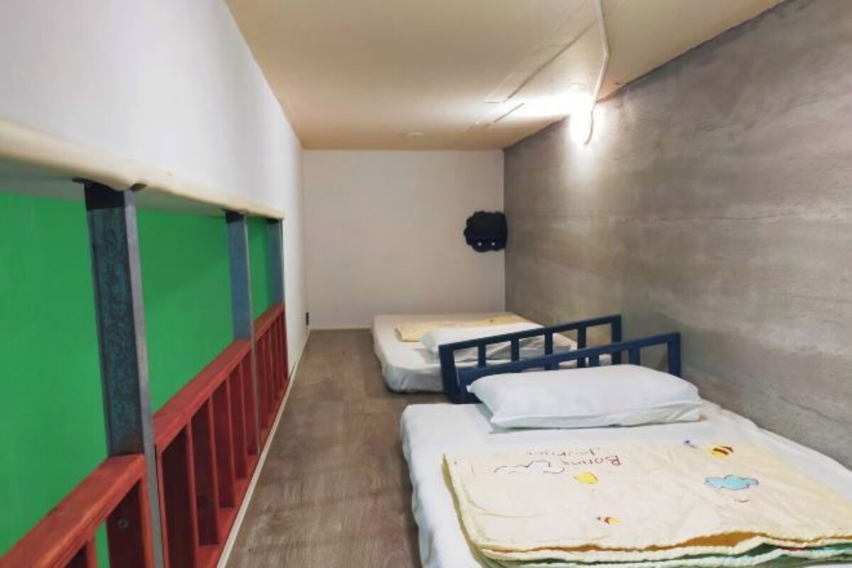 A narrow corridor with two beds, each with a blue frame and white bedding.