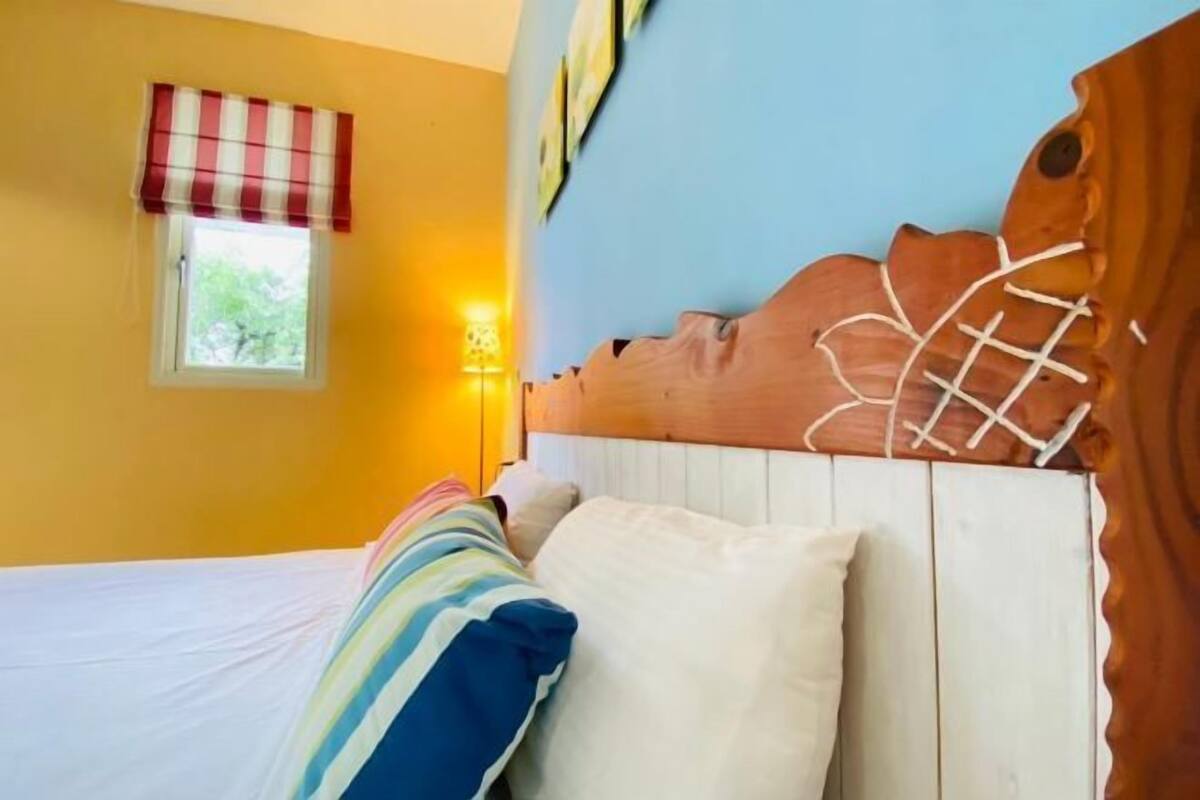 A bedroom with a bed, a window with a checkered blind, a wall lamp, and a wooden headboard with a rope design.