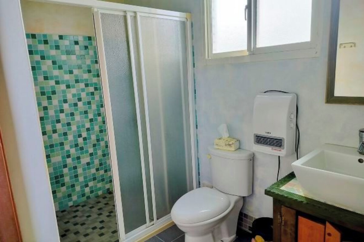 A bathroom with a toilet, a hand dryer, a sink, and a tiled shower area.