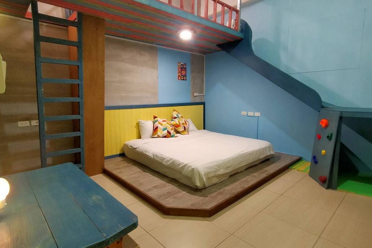 A bedroom with a bunk bed, a small desk, and a climbing wall.