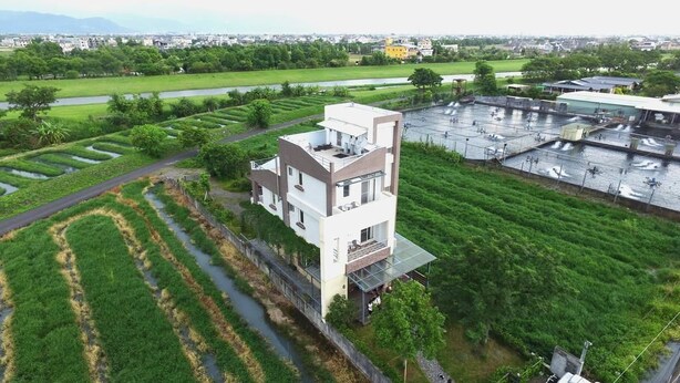 A modern building with a flat roof and a rectangular shape, surrounded by green fields and a water body. - Mei Shiou BB (Dongshan)