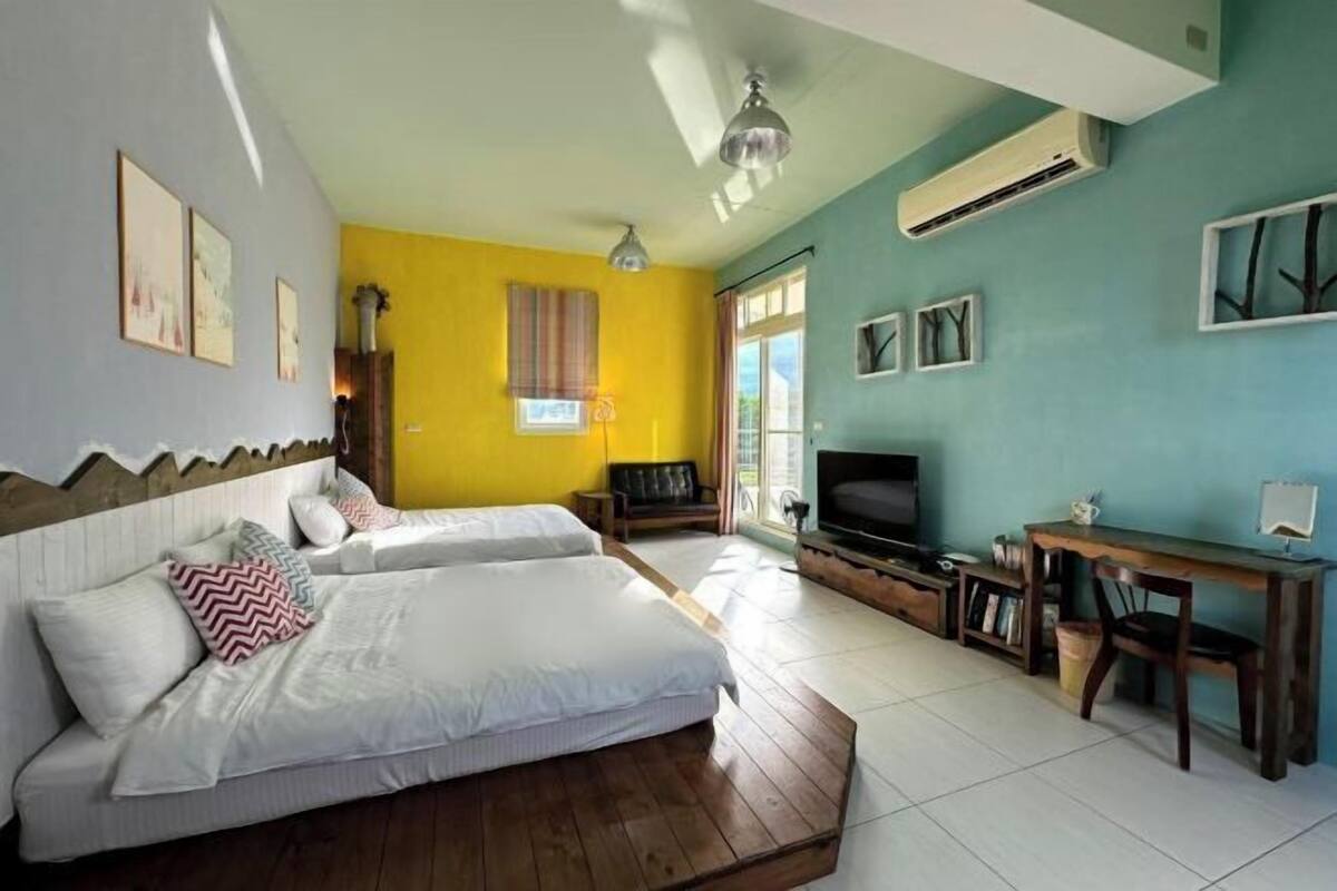A room with two beds, a TV, a desk, and a window.