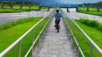 A person riding a bicycle on a concrete pathway with metal railings, leading towards a bridge over a river.