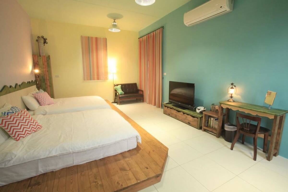 A bedroom with two beds, a TV, a desk, and a chair.