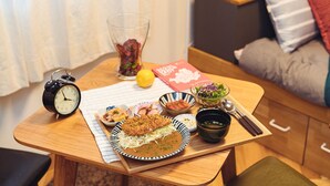 Ett matbord med en tallrik mat, ett glas vatten, en skål med sallad, en sked och en väckarklocka.