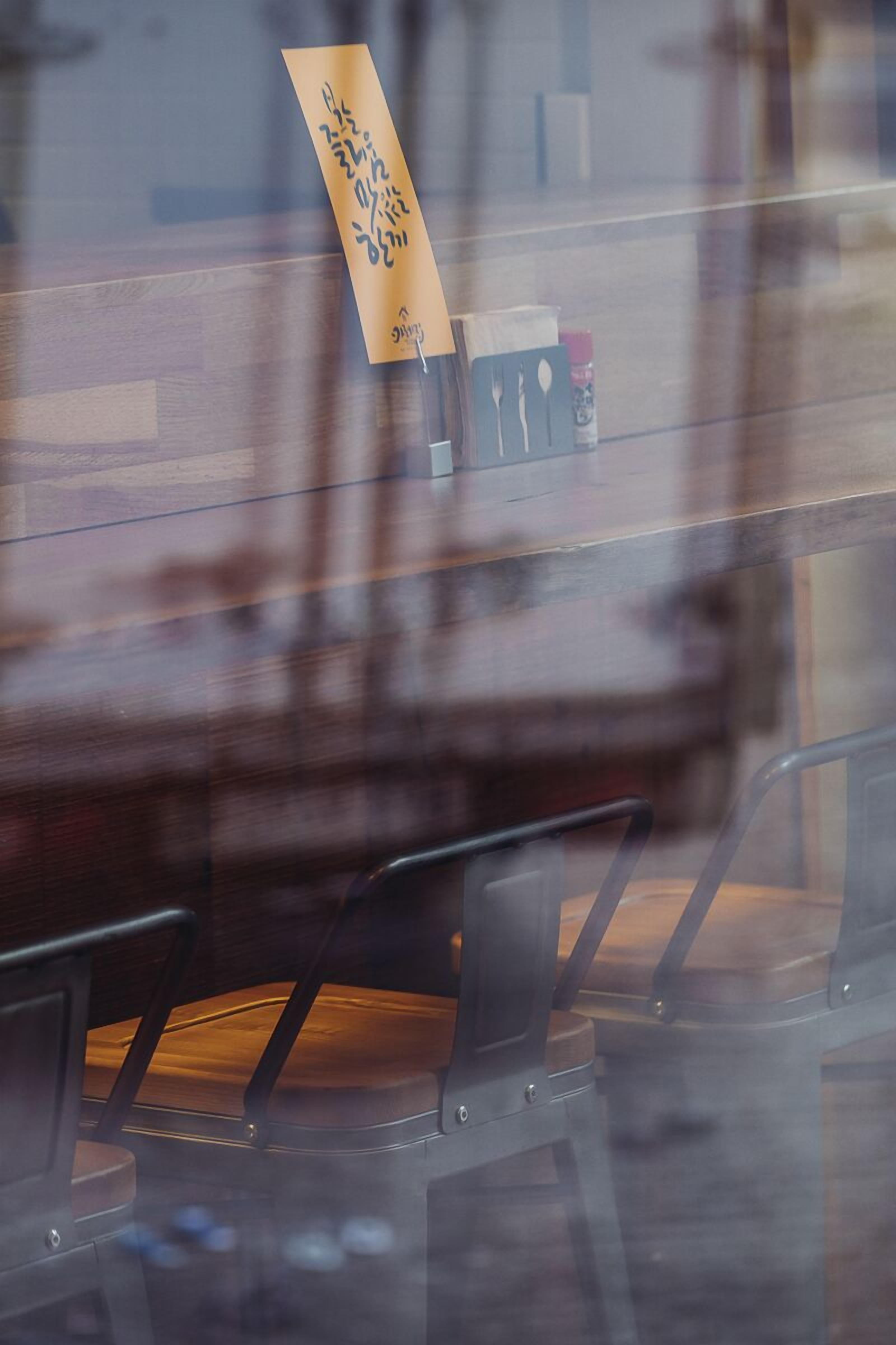 A restaurant interior with a wooden table and chairs, a menu on the wall, and a glass partition.