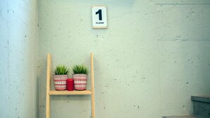Une échelle en bois, avec deux plantes en pot et une bougie rouge sur la deuxième étagère. Une pancarte au-dessus indique « 1ER ÉTAGE ».