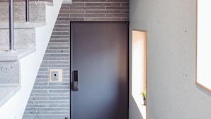 Un escalier moderne avec une finition en béton, une porte sombre et une petite fenêtre sur le mur.