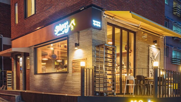 Un restaurant à la façade en briques, doté de grandes fenêtres et d’une terrasse.