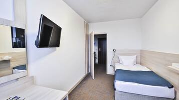 A hotel room with a bed, bedside table, a flat-screen TV mounted on the wall, and a door leading to another room.