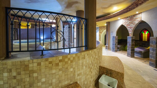 Un área de spa con piso de baldosas, un banco curvo y una pared de piedra con un vitral.