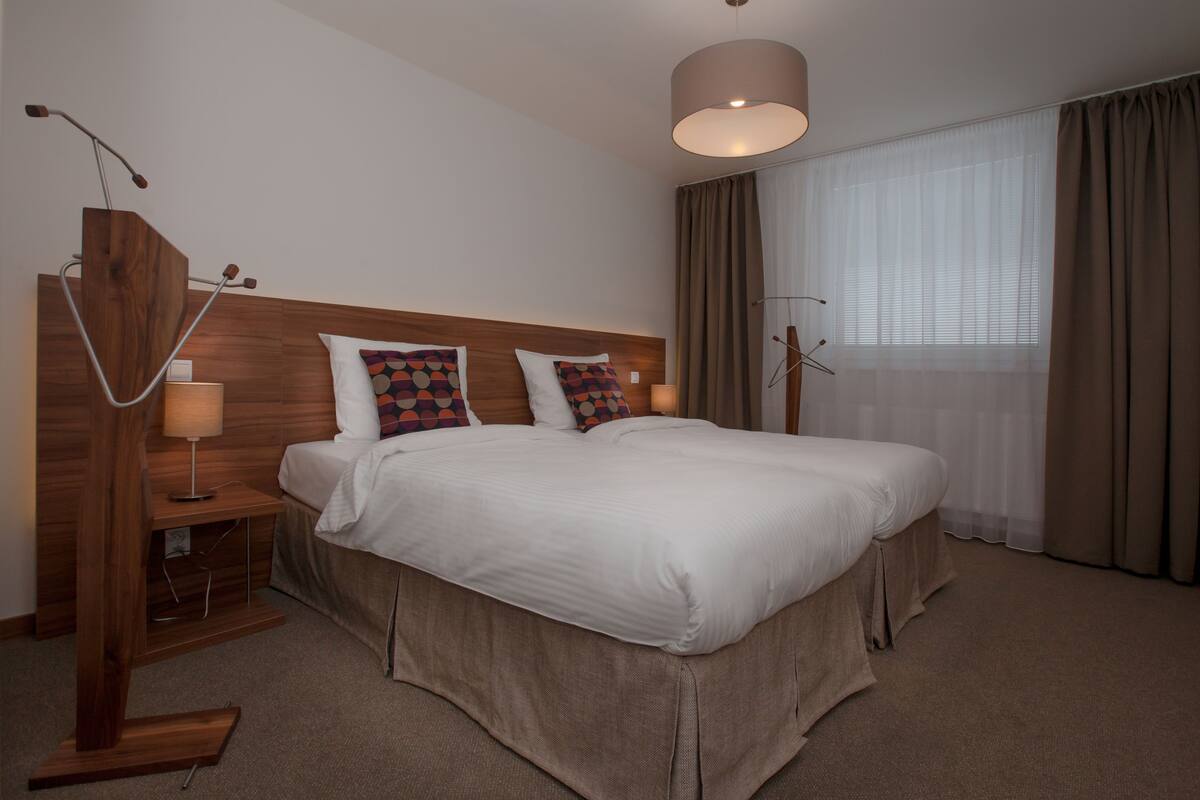 A hotel room with a large bed, a wooden nightstand, a lamp, and a ceiling light fixture.