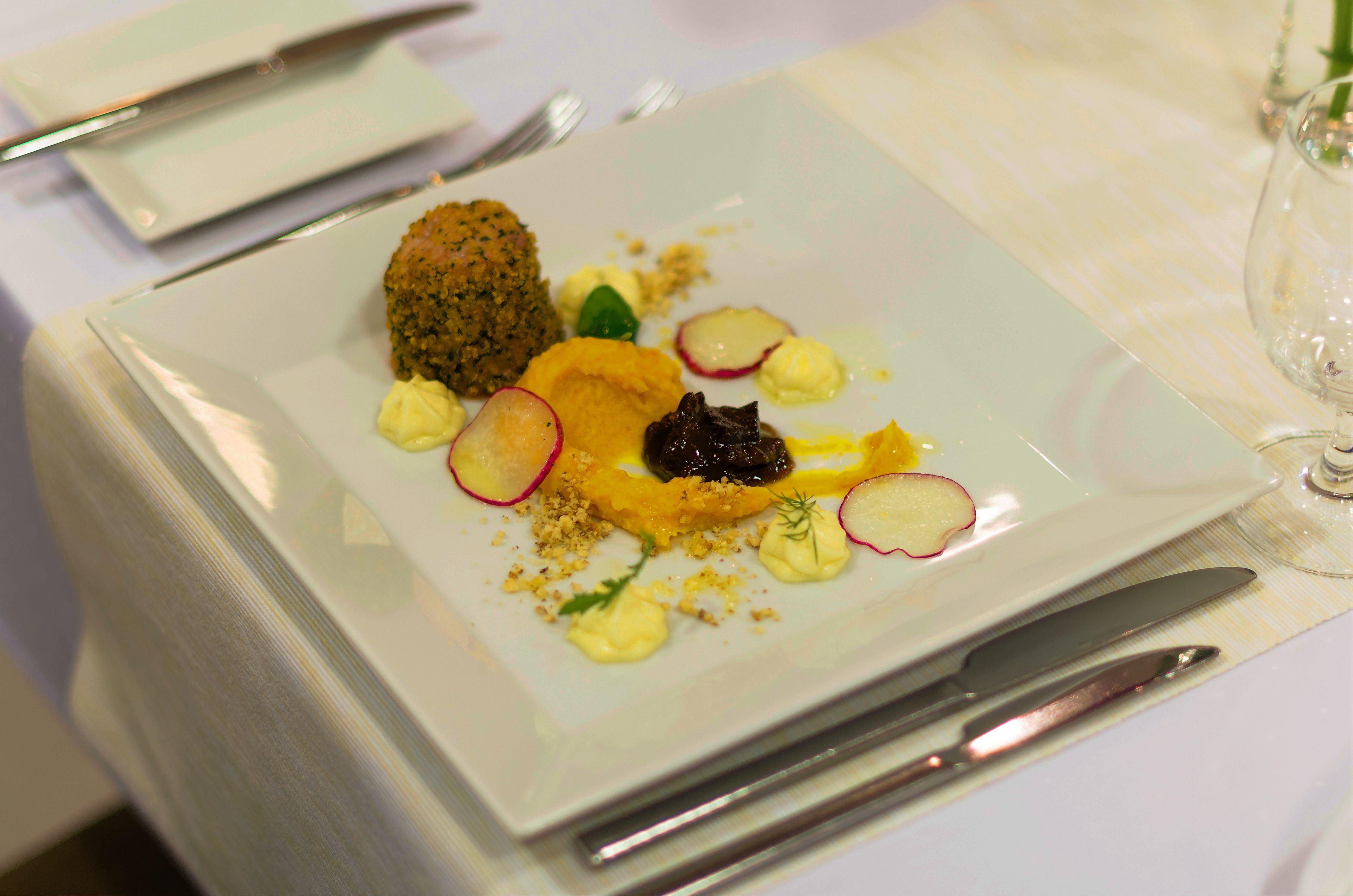 Un plato con diversos alimentos, como una preparación empanizada, un trozo de carne y guarniciones como rodajas de rábano y hierbas.