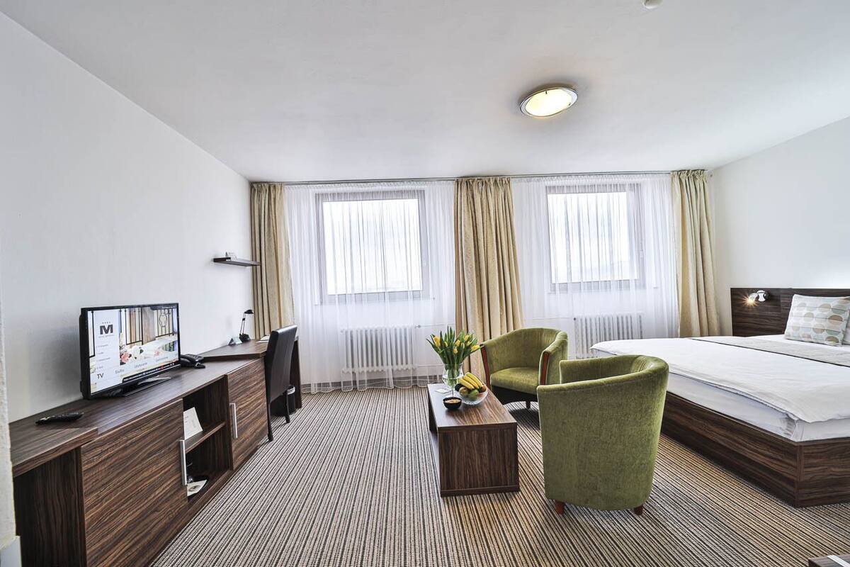 A hotel room with a bed, a desk with a TV, a chair, and a coffee table.