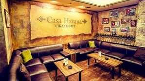 Un rincón de descanso acogedor con sofás de cuero, mesas de madera y un gran cartel en la pared que dice 'Casa Havana Cigar & Cafe'.