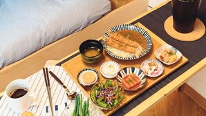 Una habitación pequeña con cama, una mesita con una bandeja de comida, televisión y una planta en maceta.