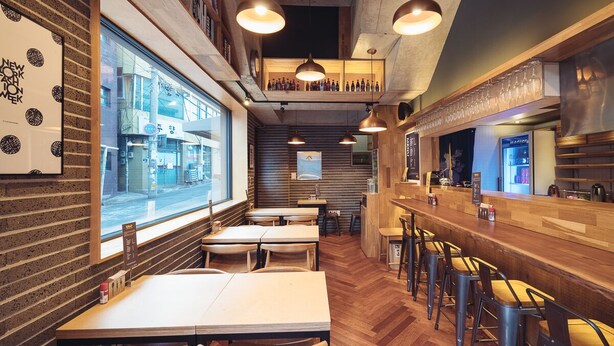Un interior de restaurante con suelo de madera, varias mesas y sillas, iluminación colgante y una zona de bar.