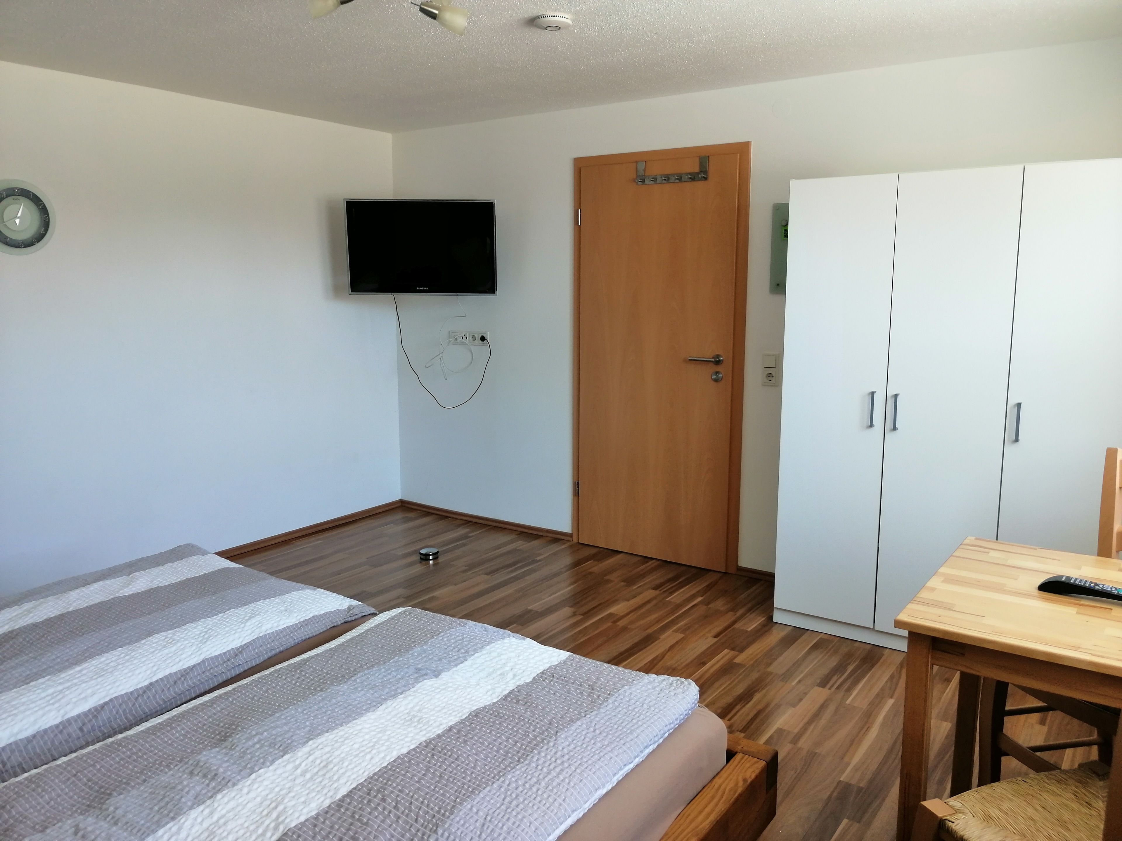 A bedroom with a bed, a TV mounted on the wall, a wooden door, and a wardrobe.