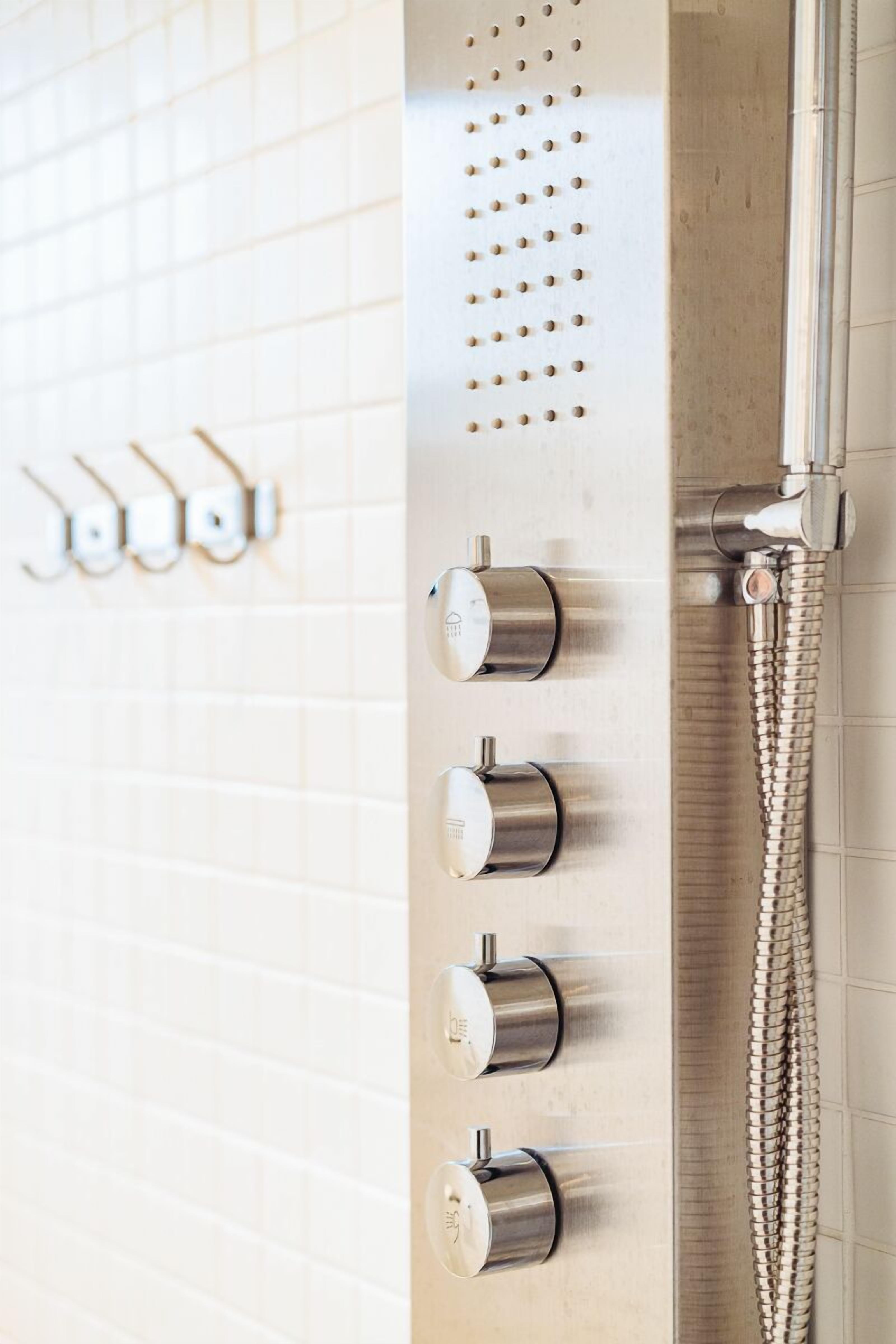 A bathroom with a wall-mounted shower control panel and a showerhead.