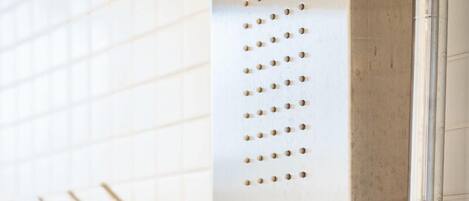 A bathroom with a wall-mounted shower control panel and a showerhead.