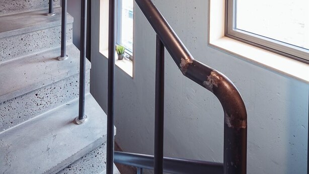 Una escalera con escalones de hormigón y barandillas de metal negro, que conduce a una habitación con ventana y vistas al exterior.