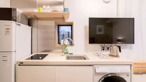 Una kitchenette compacta con microondas integrado, un lavamanos pequeño, lavavajillas y un televisor montado en la pared.