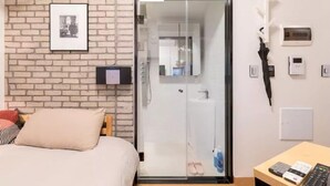 Habitación de hotel con pared de ladrillo, cama con almohada color beige, puerta de vidrio corredera que da a un baño y una mesa con un control remoto.