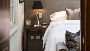 A hotel room with a bed, bedside table, lamp, and a window with curtains. - Private Knightsbridge Mews House | Harrods 1min, Parking & Top 5% Rated (Knightsbridge)