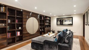 A modern living room with a large bookshelf, a round mirror, and a grey sofa. - Private Knightsbridge Mews House | Harrods 1min, Parking & Top 5% Rated (Knightsbridge)
