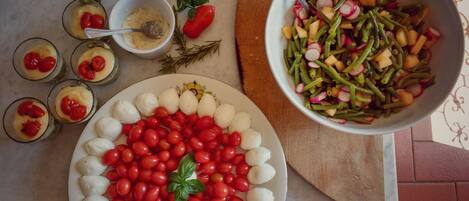 A table with a plate of mozzarella balls and cherry tomatoes, a bowl of green beans and radishes, and small glasses of a creamy dessert with cherries.