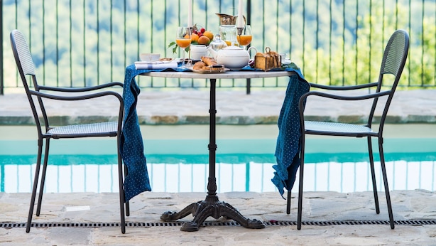 Ein Tisch reichhaltig mit Frühstück gedeckt, mit Früchten, Gebäck und Getränken, mit Blick auf einen Pool.