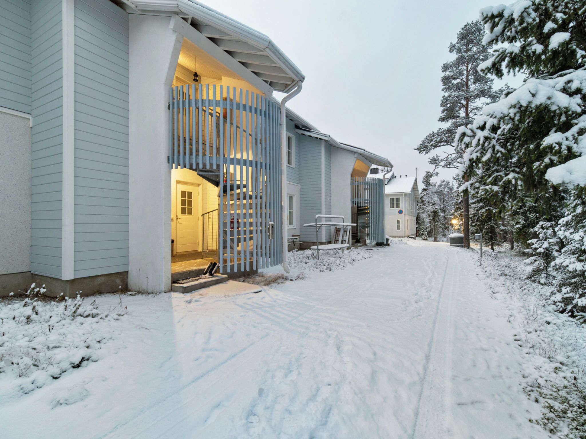 A snow-covered residential area with a house featuring a visible staircase and a gated entrance.