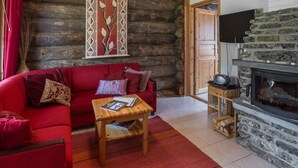 A cozy log cabin interior with a red sofa, a wooden coffee table with magazines, a stone fireplace, and a wall-mounted artwork.