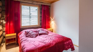 A bedroom with a large bed, red curtains, a wooden headboard, a nightstand, and a window with blinds.